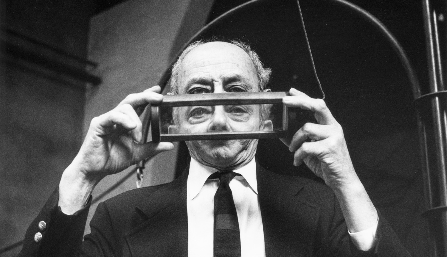 Photo of an older man holding a framed, transparent prism, which partly blocks and distorts his face.