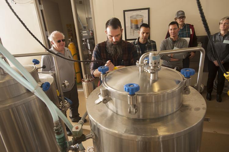 Students and teachers stand around beer tanks during a brewing class.