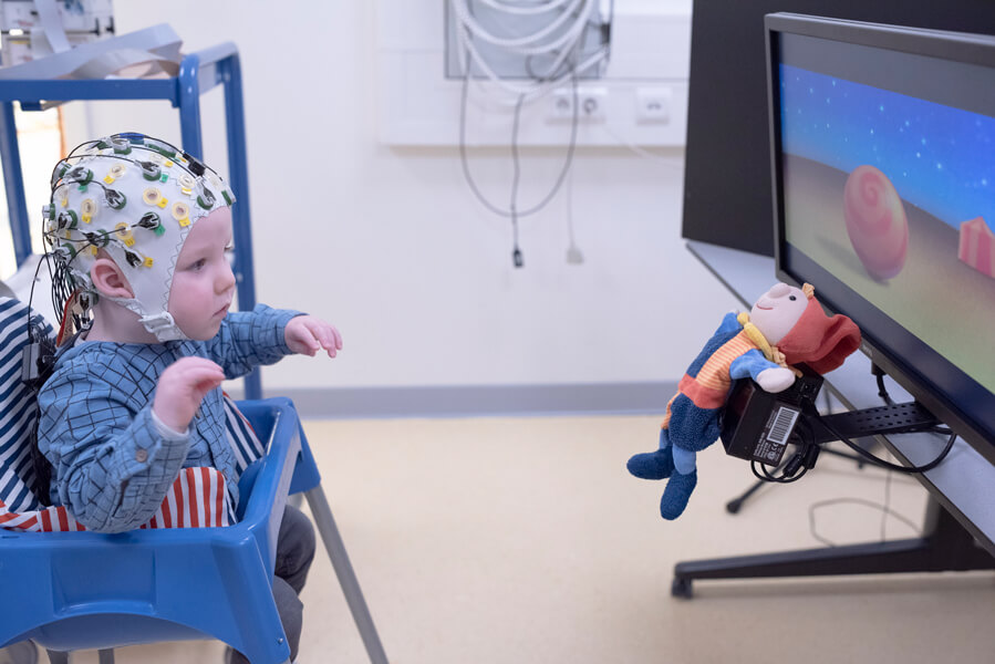 An image of an infant with a net of sensors on its head watching a television screen.