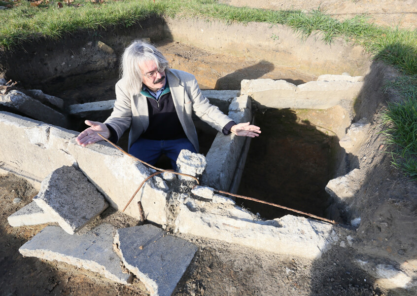 Photograph of Reinhard Bernbeck at the archaeological site at Tempelhof. Bernbeck is positioned in the entrance to a former air raid shelter of a Lufthansa forced labor camp.