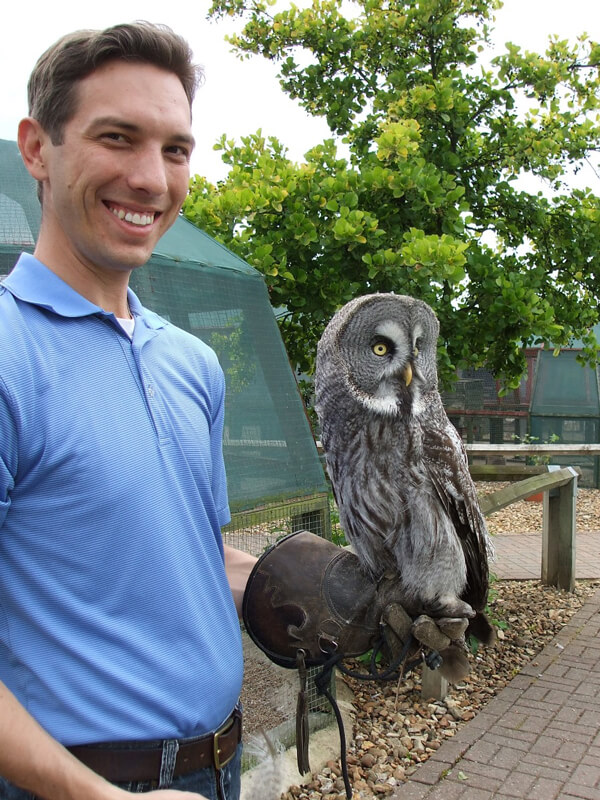 Photo shows Justin Jaworski smiling as a large owl perches on his gloved hand.