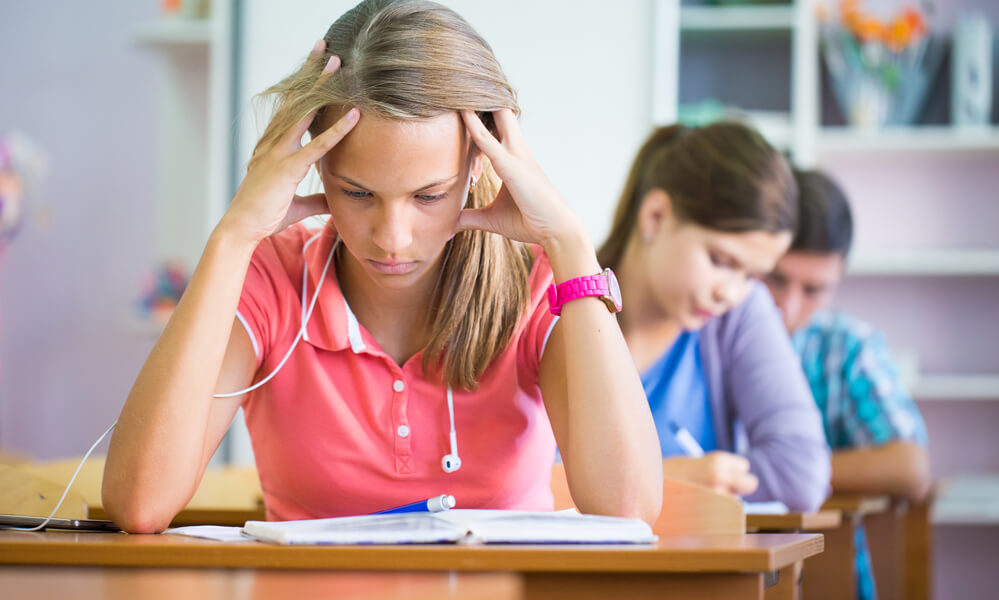 Photo shows a girl in middle school classroom frowning as she concentrates on an assignment on desk.