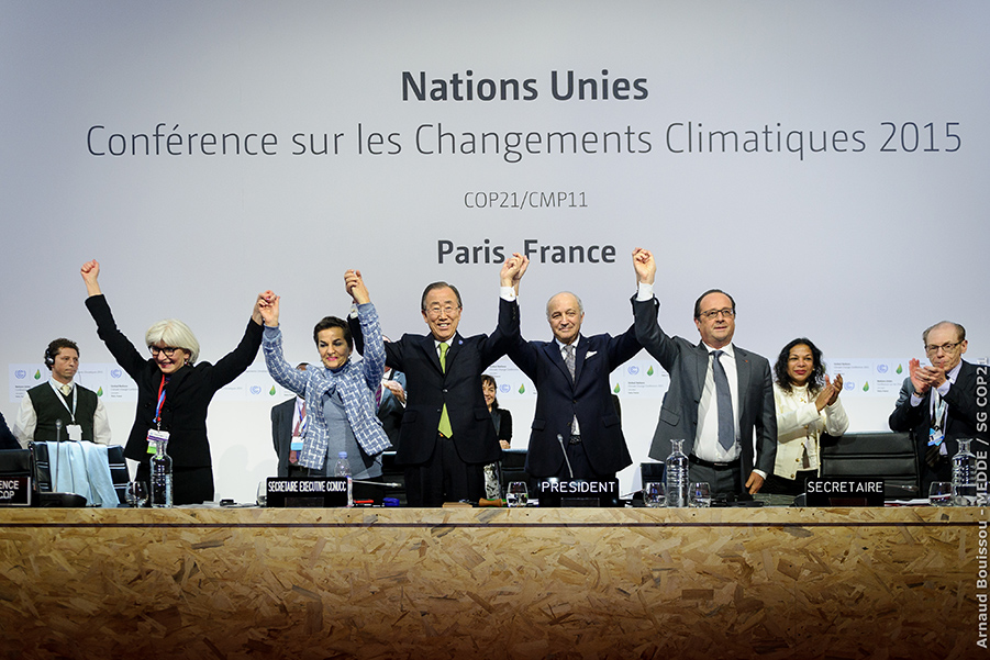 Photo shows UN leaders and others with hands grasped in celebration below a sign, in French, for the global meeting on climate change.