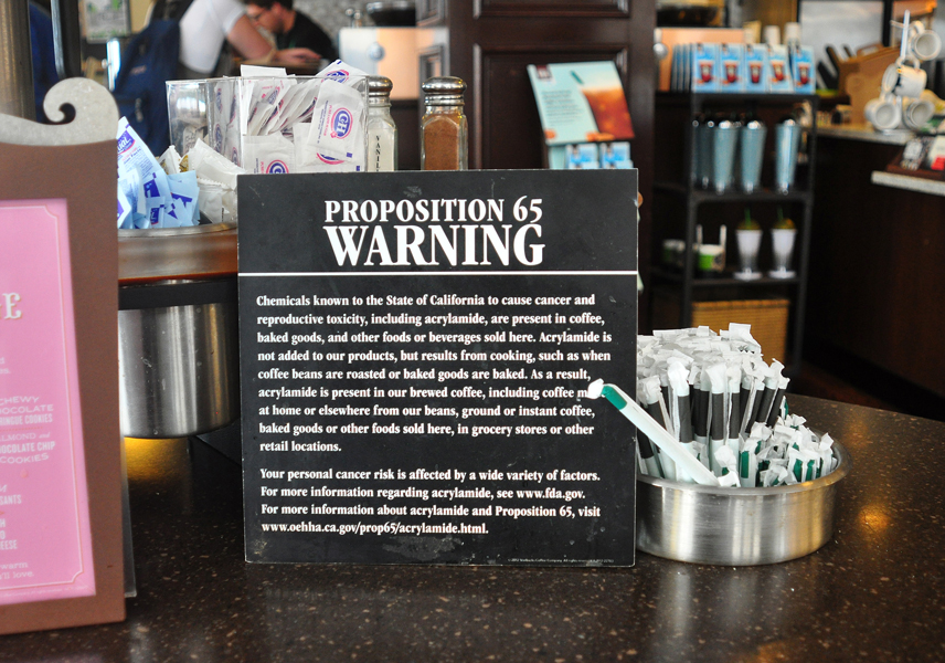 A Proposition 65 sign in a San Francisco Starbucks warns of acrylamide in coffee and baked goods. It is located by the sugar and creamer; Starbucks was sued to place the warning at the point of sale.