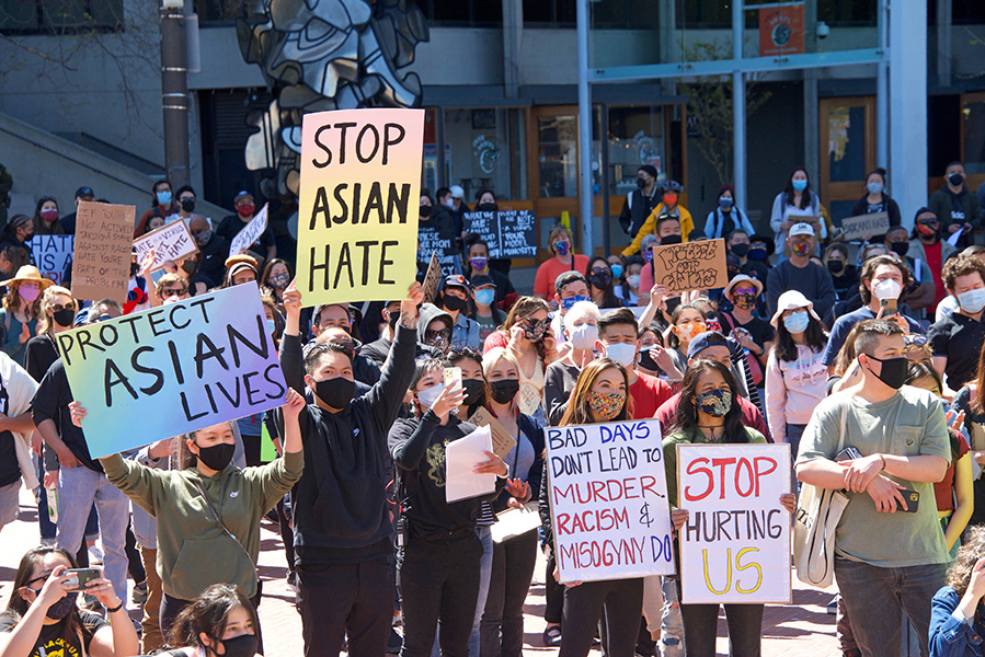 A photograph shows people demonstrating against Asian racism and hate crimes. They are carrying signs that read “Protect Asian lives,” “Stop Asian hate” and “Stop hurting us.”