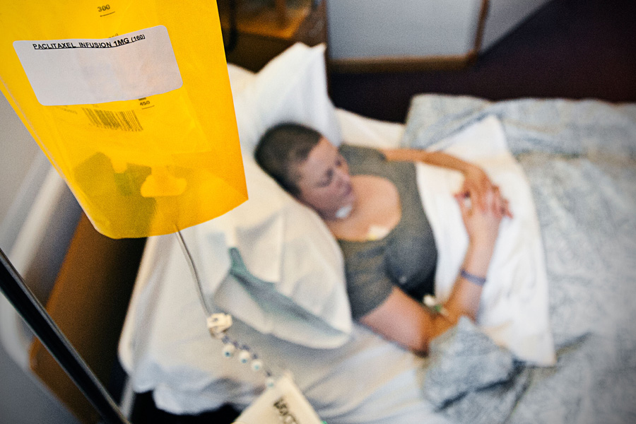 Photograph of a woman lying in a hospital bed receiving an infusion of paclitaxel from a yellow-colored bag.