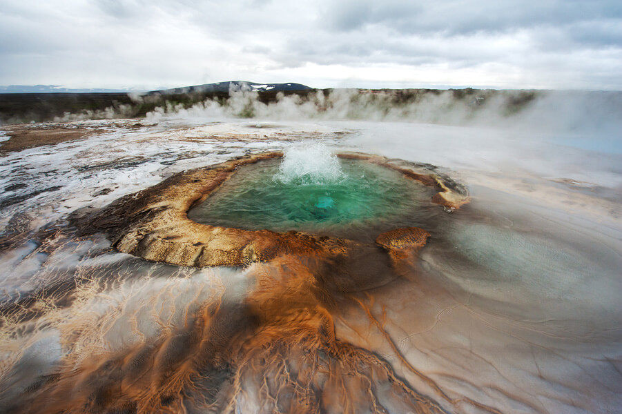 A bubbling pool surrounded by muddy brown streaks and steam. 