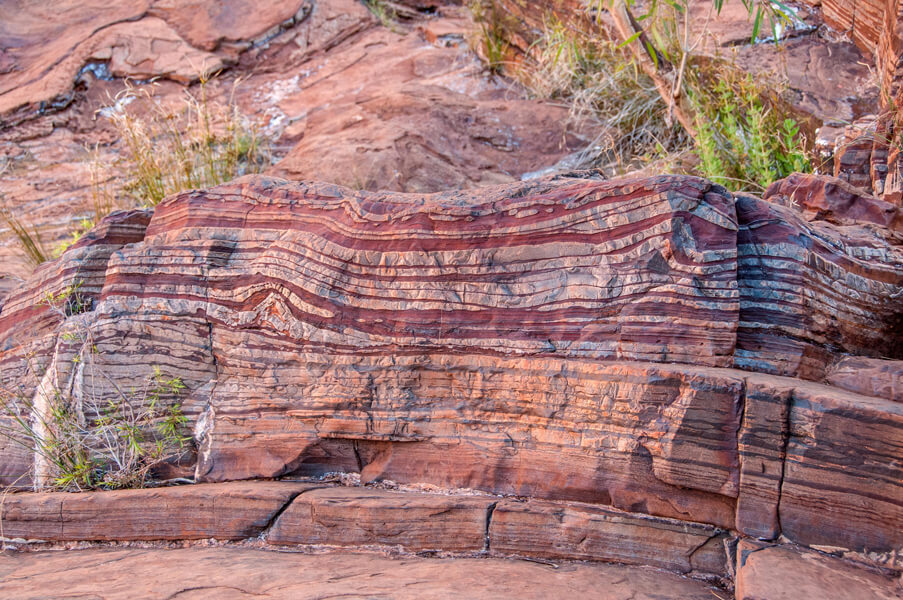 Photo shows a reddish sedimentary rock with alternating layers of different hues.