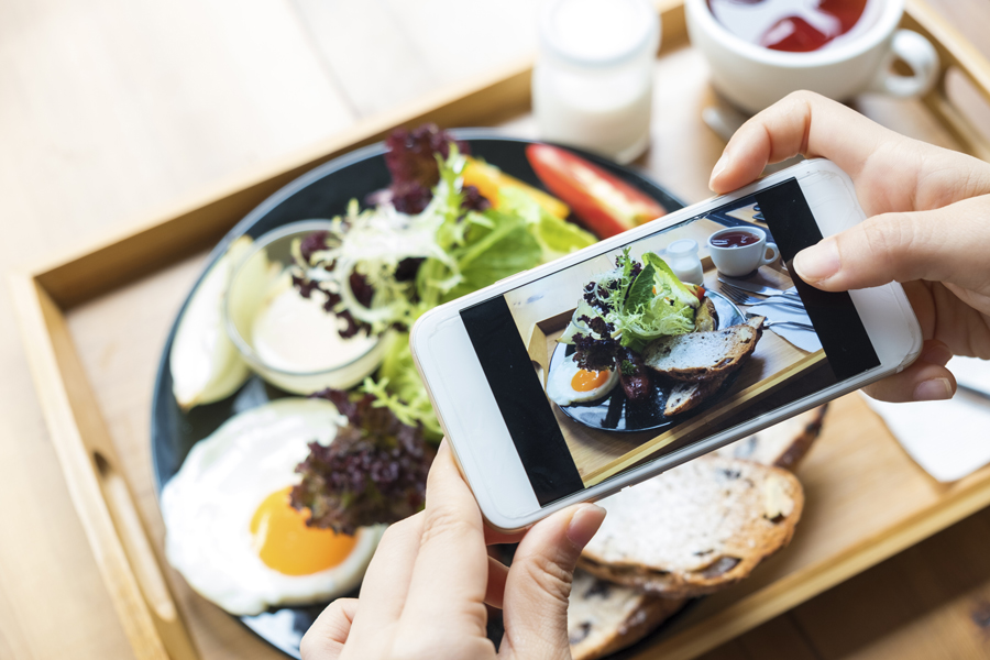 Image shows a smart phone hovering over a plate of eggs, toast and salad. The phone is taking a photo of the meal.