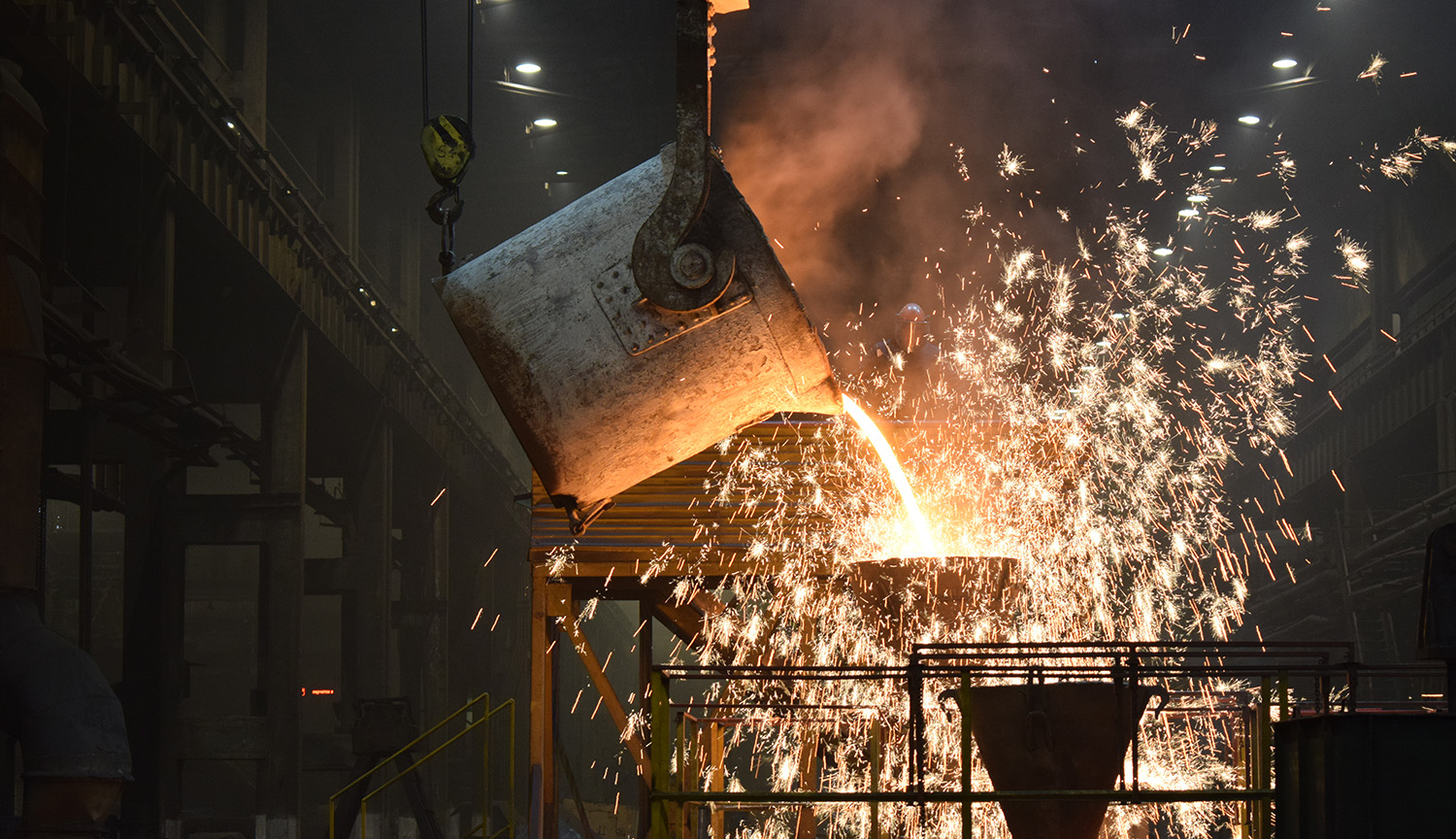 Photograph of molten metal being poured from a bucket in a metal workshop