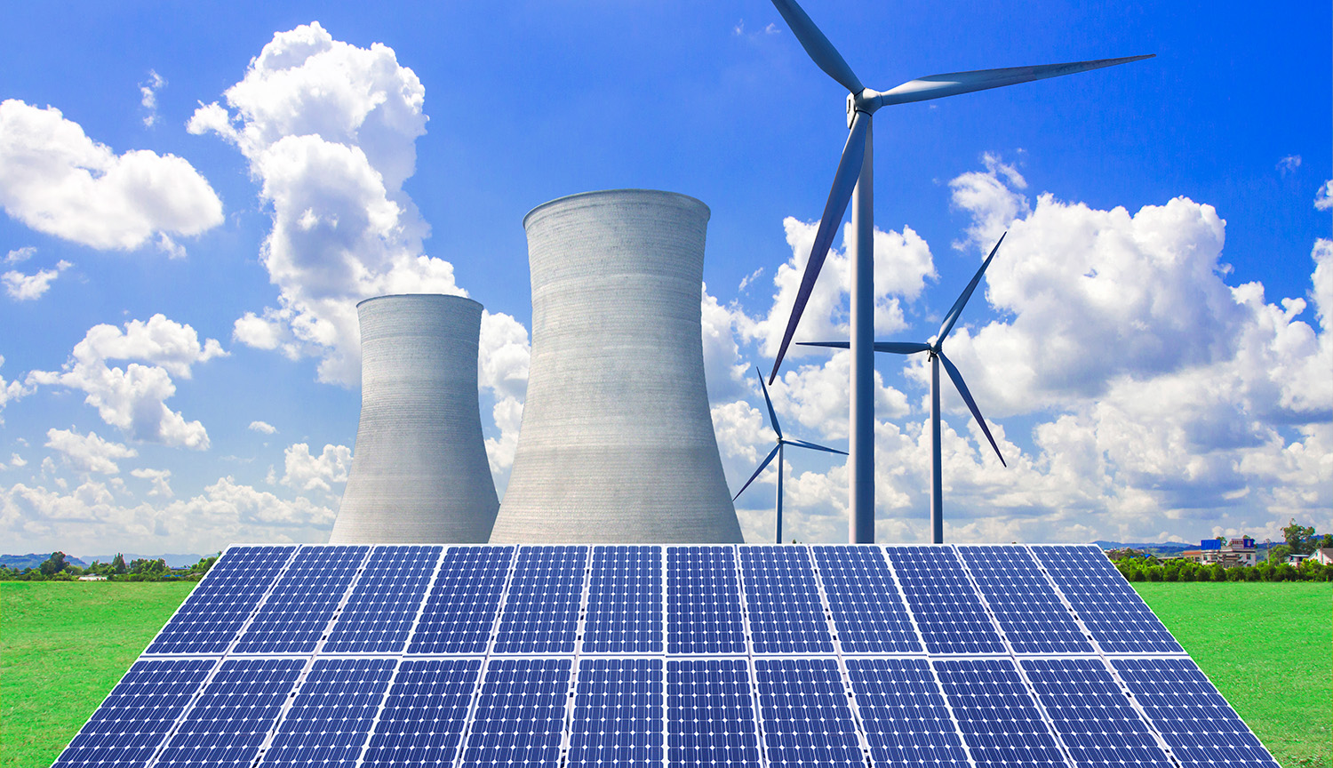 The cooling towers of a nuclear power plant rise above an array of solar panels, with wind turbines also visible