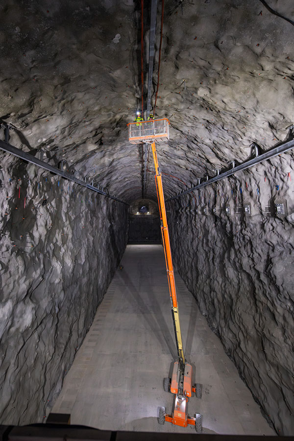 Underground lab Workers on a hoist inspect the walls of a large tunnel.