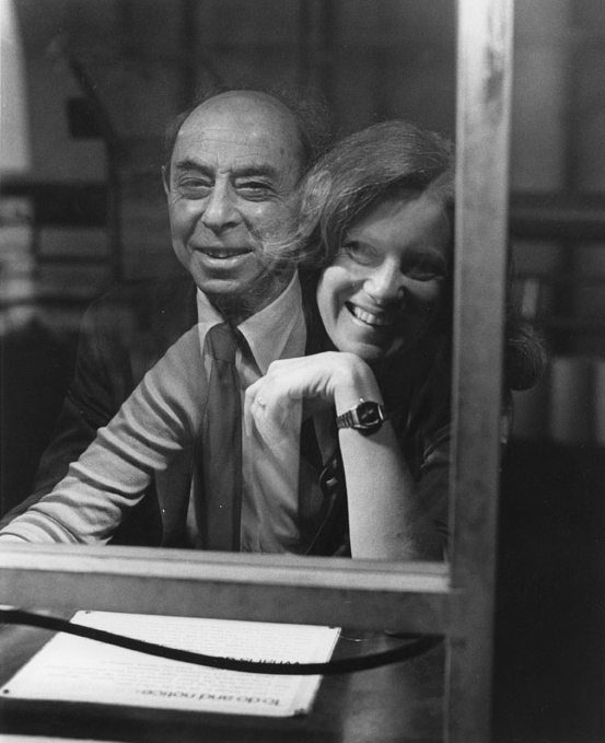 A photo shows the reflection of a woman laughing next to the image of a smiling man who sits opposite to her as they interact with an exhibit that takes advantage of changing light levels and a kind of two-way mirror.