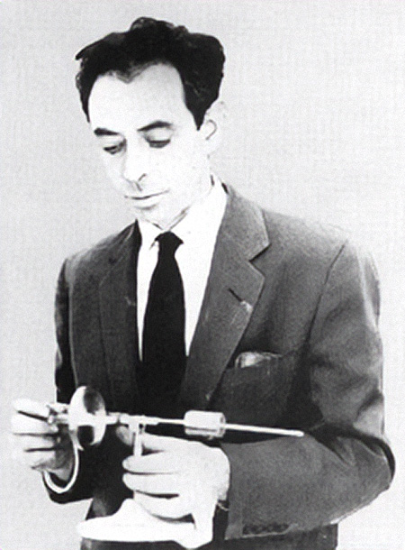 A black-and-white photo shows a young man in a suit and tie glances down at the instrument in his hand.
